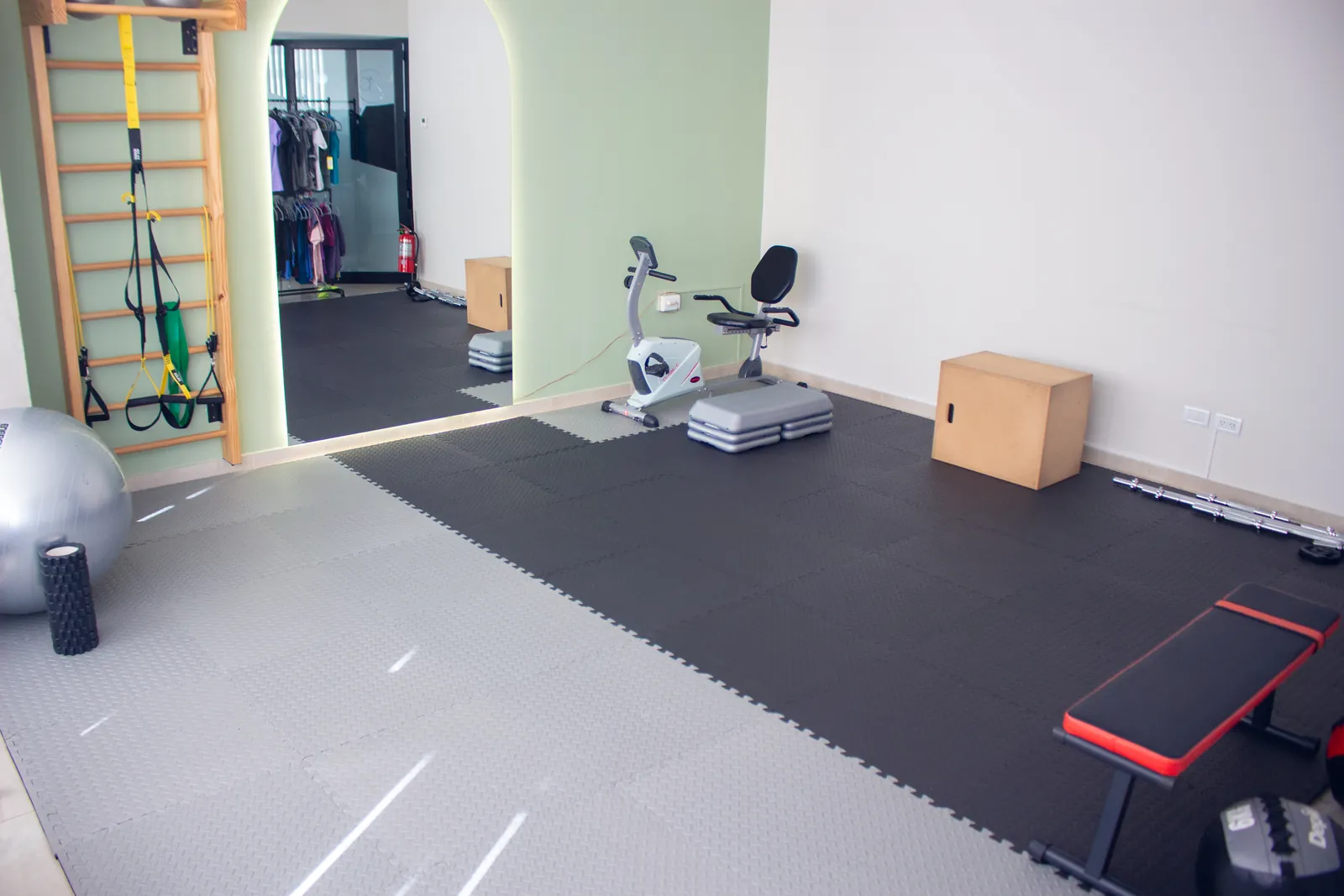 Sala de ejercicio con piso de goma, bicicleta fija, banco y espaldar