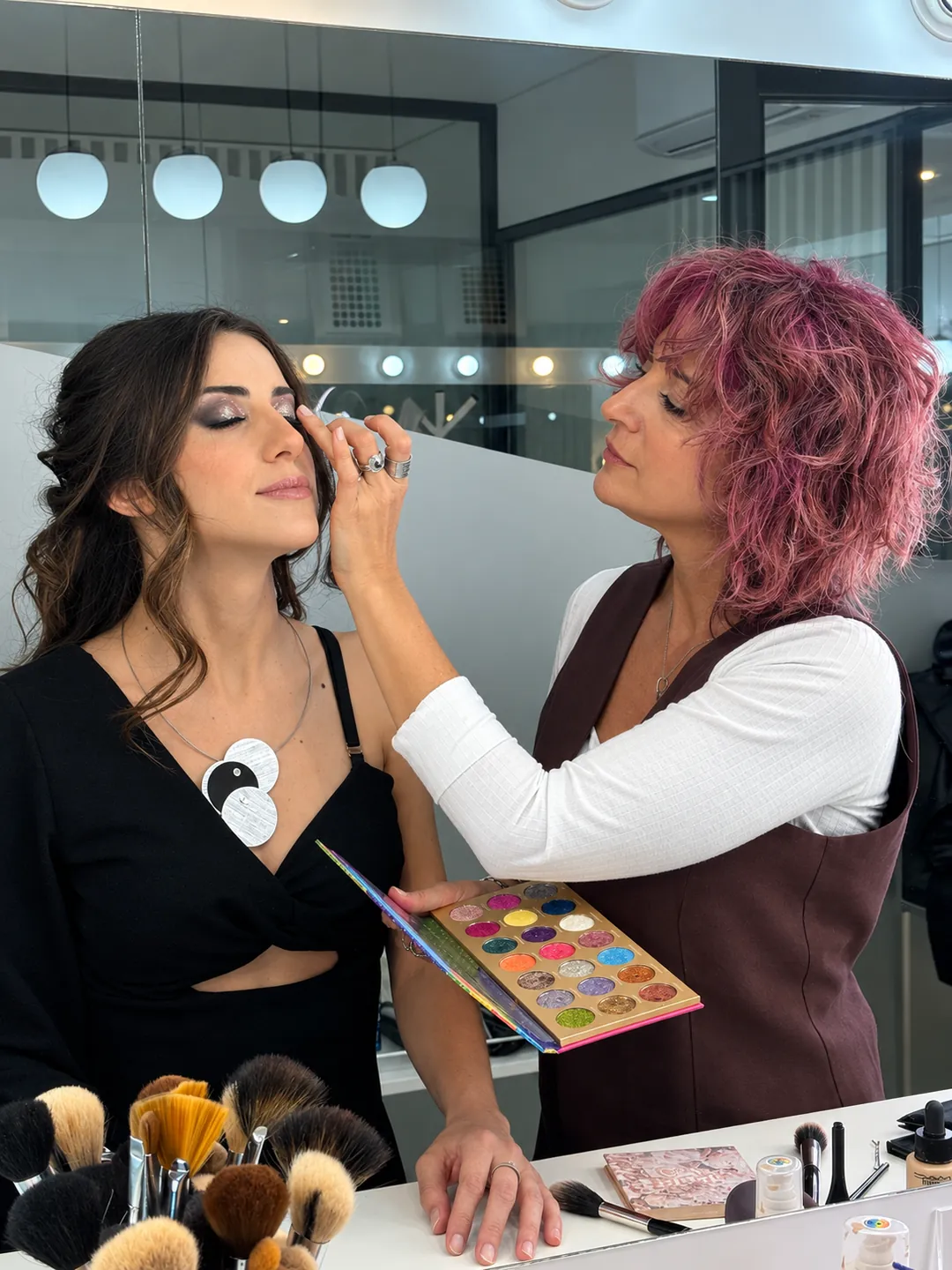 Andrea Guevea maquillando los ojos de una clienta frente al espejo con luces
